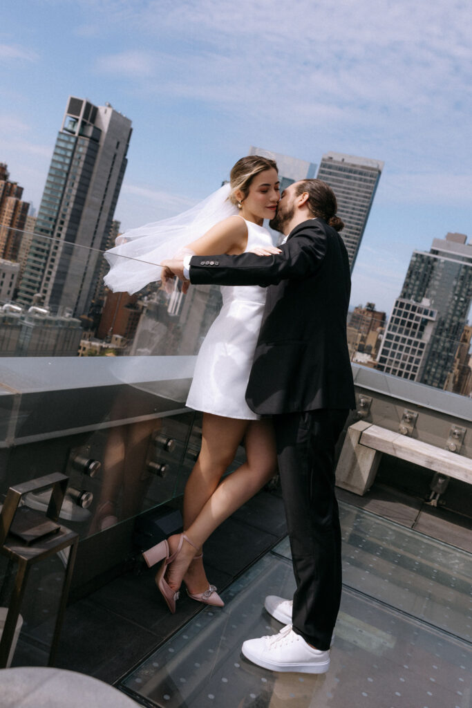 Couple sharing a tender neck kiss on a rooftop with sweeping city views, capturing a romantic and intimate pre-wedding moment.