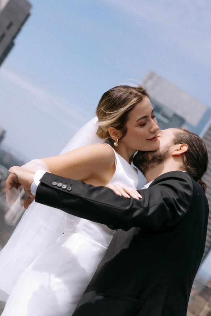 A close-up of a bride and groom sharing a tender embrace on a rooftop, with the bride smiling softly and the NYC skyline in the background.