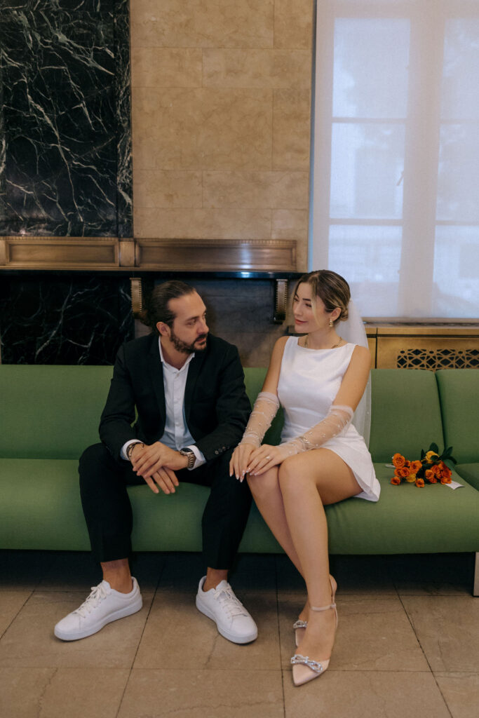 Couple sitting on a green couch inside Manhattan City Hall, capturing a calm and intimate moment before their wedding ceremony