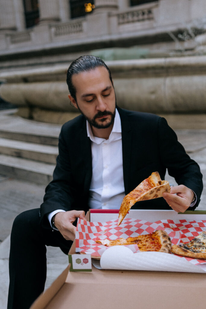 Couple sharing a delicious pizza meal outside the New York Public Library, capturing a joyful moment in their NYC elopement celebration.