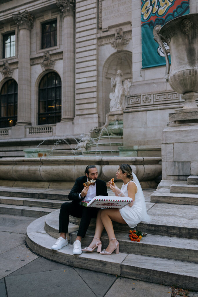 Newlyweds savoring pizza together near the New York Public Library, enjoying a relaxed and memorable moment in the heart of NYC