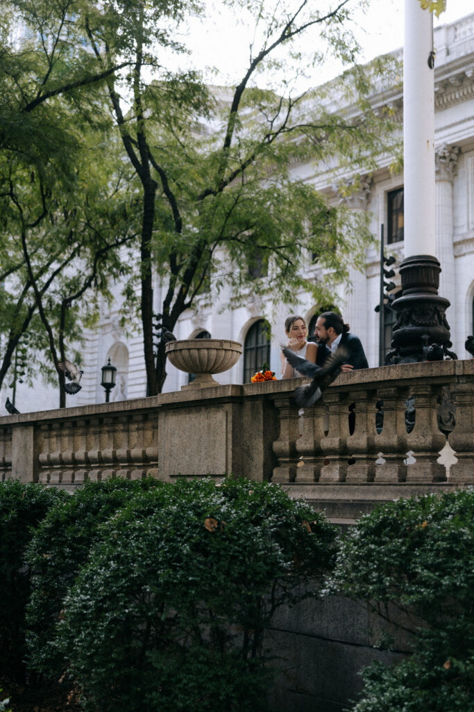 Just married couple standing by the New York Public Library as a dove flies by, capturing a magical moment on their wedding day.