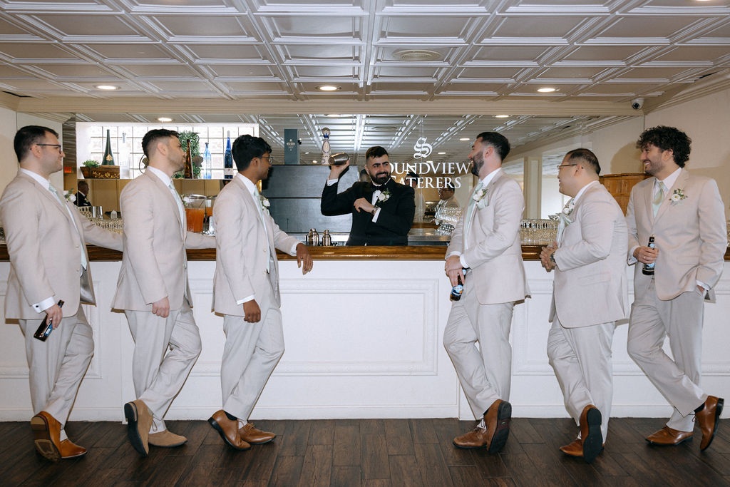 Groom and groomsmen posed with drinks at the bar, sharing laughter and camaraderie before the wedding celebration, showcasing a mix of candid and posed photography
