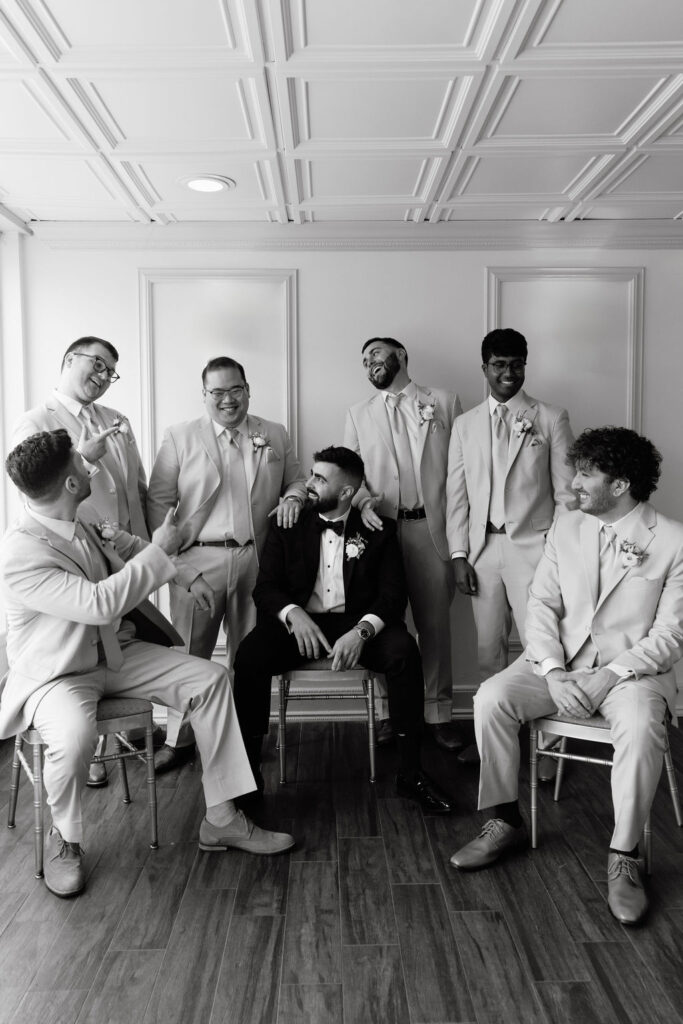 Groomsmen posed in a relaxed, candid shot with the groom, enjoying a casual moment before the wedding, featuring a mix of fun and formal styles.
