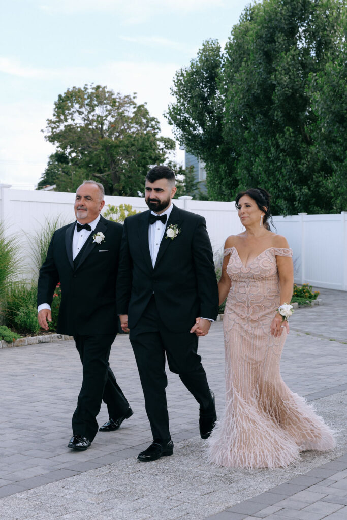 Groom walking down the aisle with his parents, captured in a heartfelt, candid moment before the wedding ceremony begins.