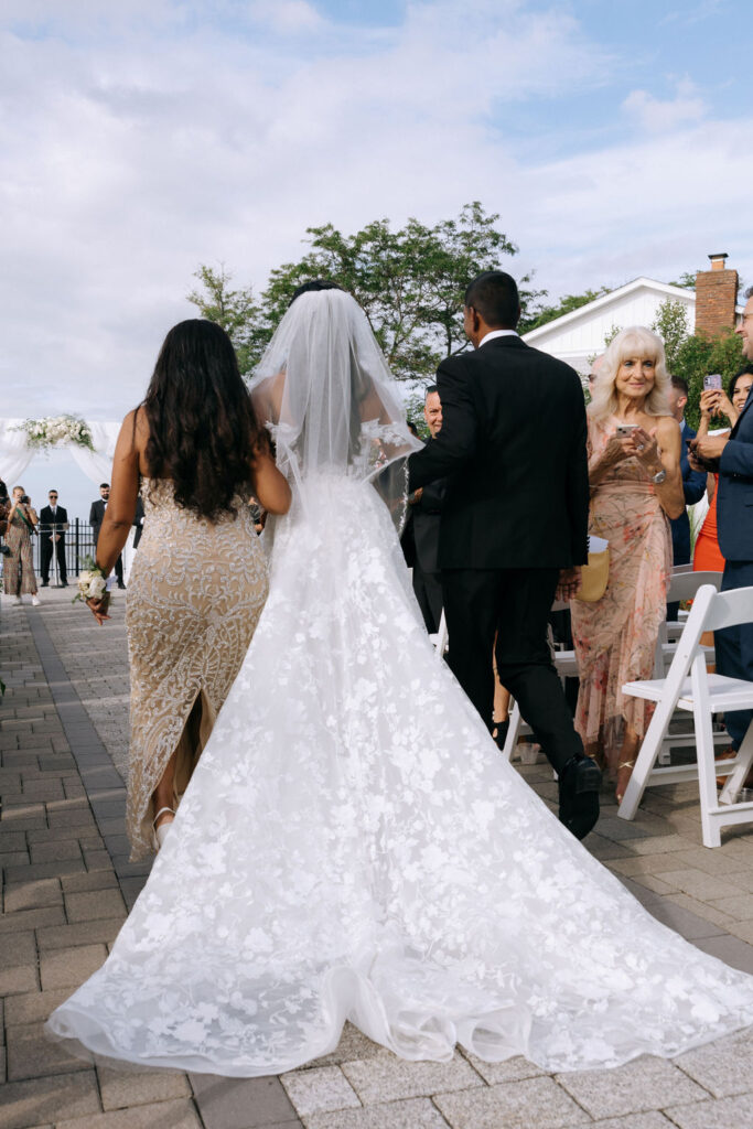 Bride walking down the aisle with her parents, sharing an emotional and joyful moment before the wedding ceremony, captured in a candid and heartfelt shot
