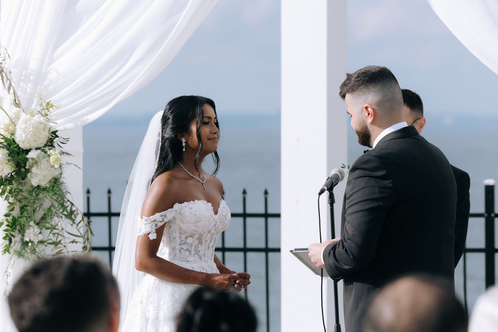 Intimate waterfront wedding ceremony with the couple exchanging vows, set against a scenic water view, capturing the romantic and serene atmosphere