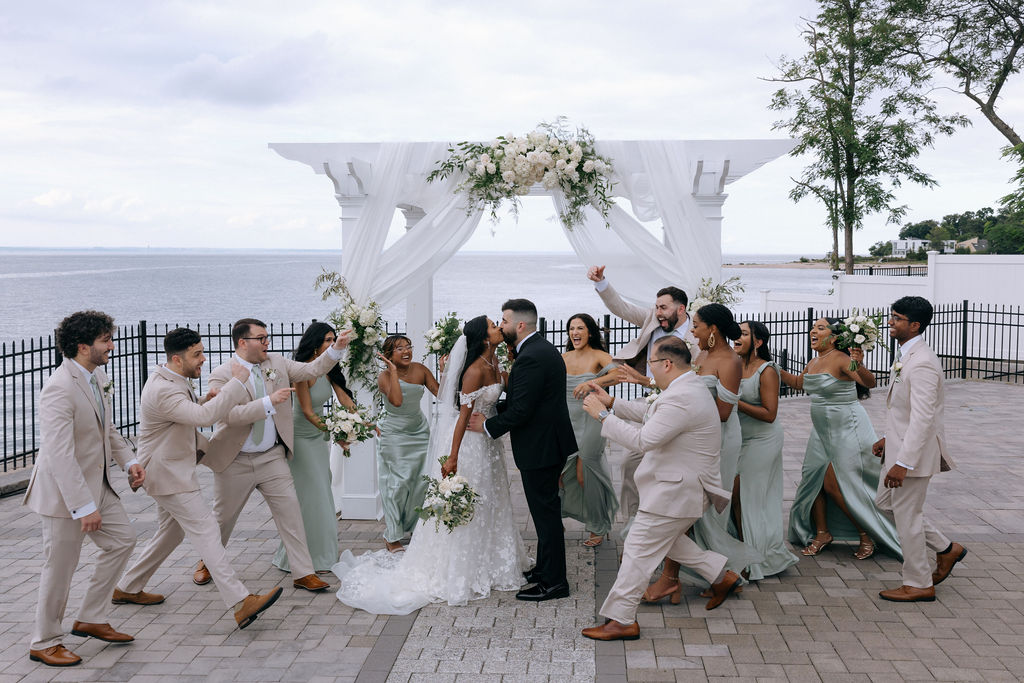 Playful bridal party shot with the bride and groom at the center, surrounded by their laughing friends, captured in a relaxed and candid moment
