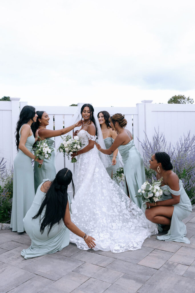 Bride surrounded by her bridesmaids, holding floral bouquets and posed in a fun, celebratory group shot before the intimate wedding ceremony