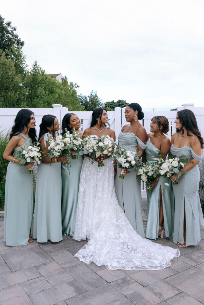 Bride and bridesmaids elegantly posed with bouquets, showcasing their close bond in a mix of candid and traditional wedding photography styles.
