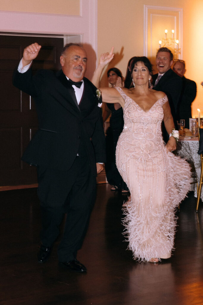 Parents joyfully entering the wedding reception, sharing smiles and excitement as they are welcomed by guests