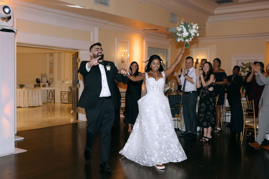 Bride and groom making a joyful entrance to the wedding reception, smiling and celebrating as they are welcomed by cheering guests
