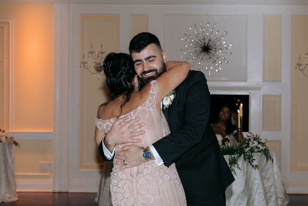 Groom dancing with his mother, while his father looks on with pride and emotion, capturing a heartfelt family moment during the wedding celebration