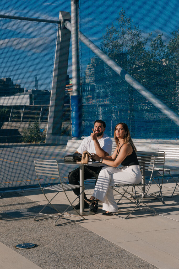 The future Bride and Groom seated at a pierside table in NYC, enjoying a candid moment as the Groom points at a plane overhead carrying a message.