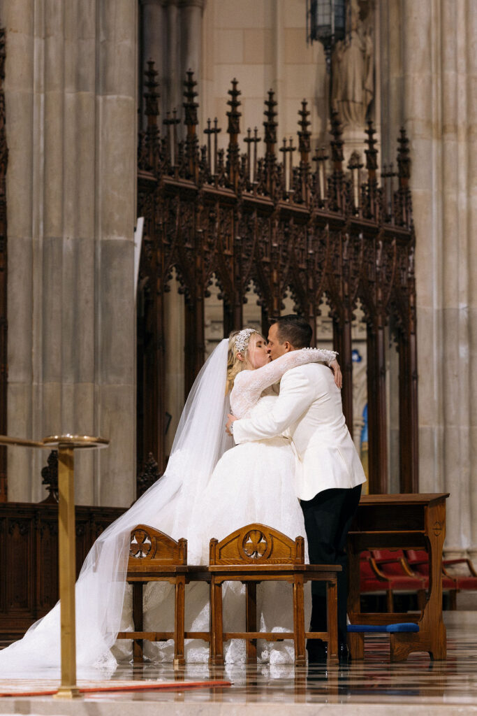 The bride and groom share their first kiss at the altar during their luxurious NYC cathedral wedding ceremony.