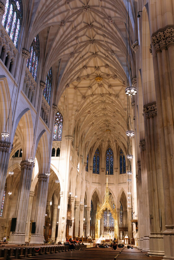 The intricate vaulted ceilings and golden altar of a grand NYC cathedral during a wedding ceremony.