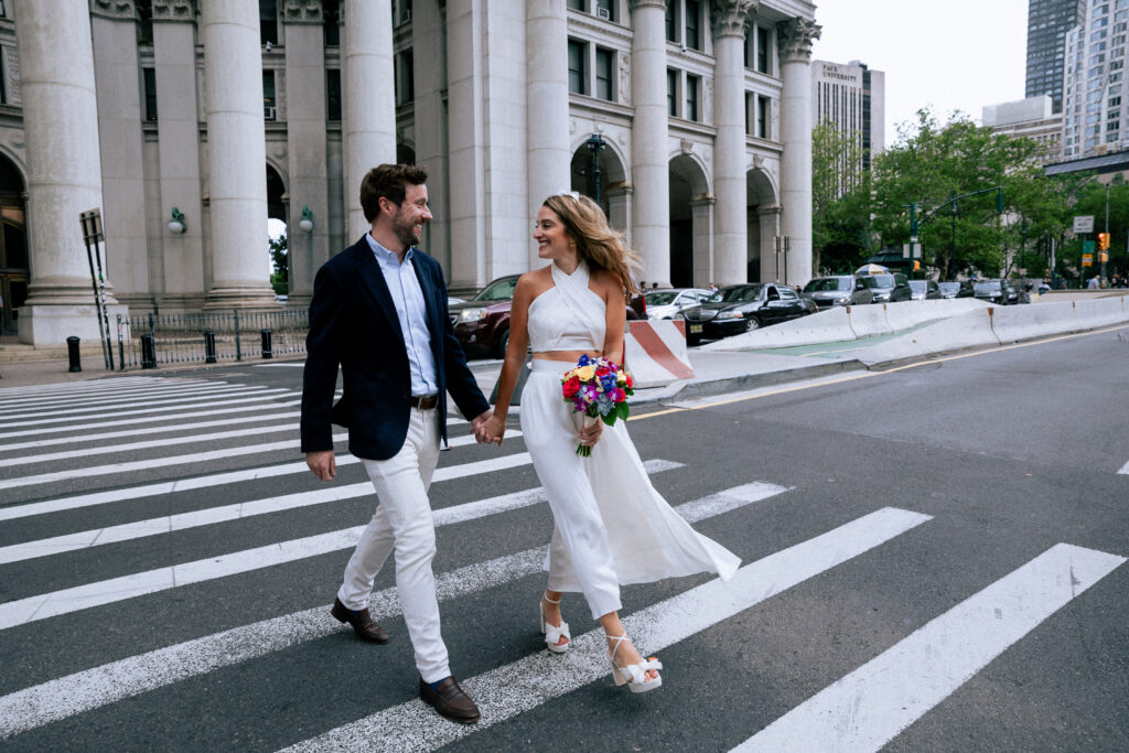 Bride and groom walking hand-in-hand across a NYC crosswalk after their City Hall wedding.