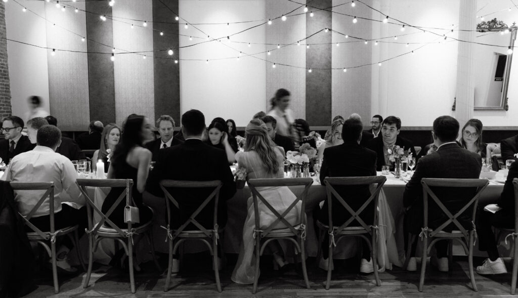 Guests seated at a long table with string lights during a wedding reception in NYC.