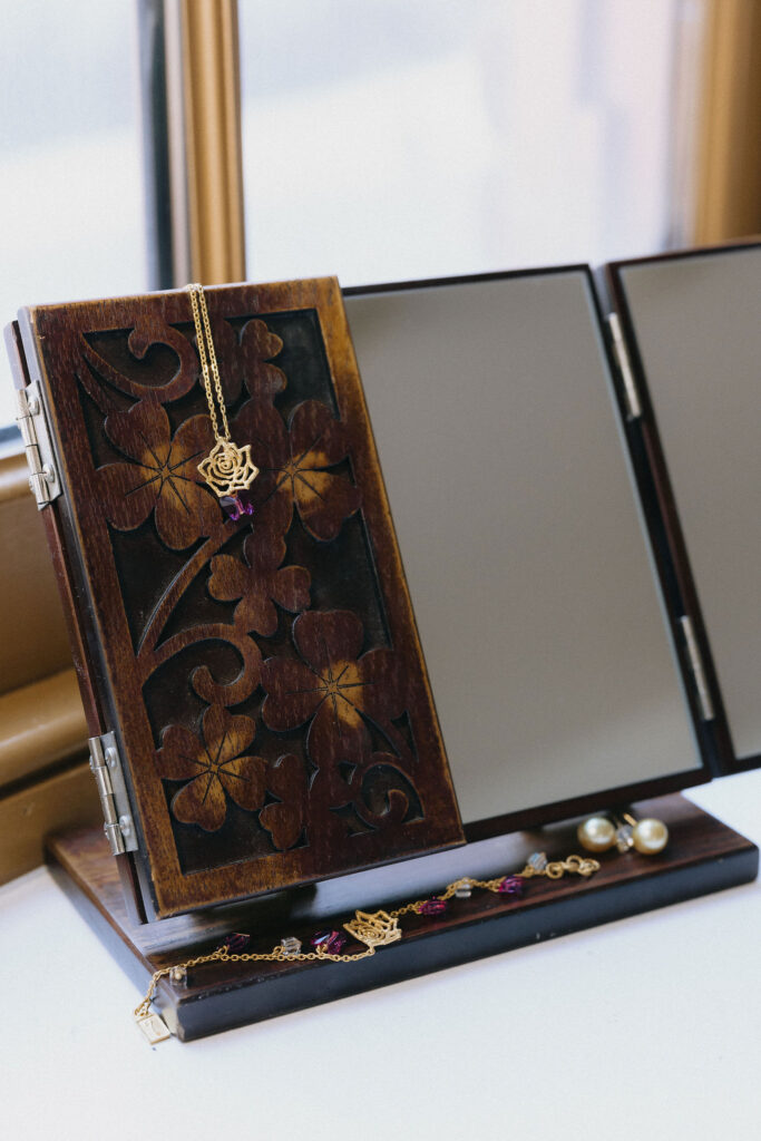 An intricately designed wooden jewelry box with floral carvings, holding a delicate gold necklace featuring a rose pendant and purple gemstone