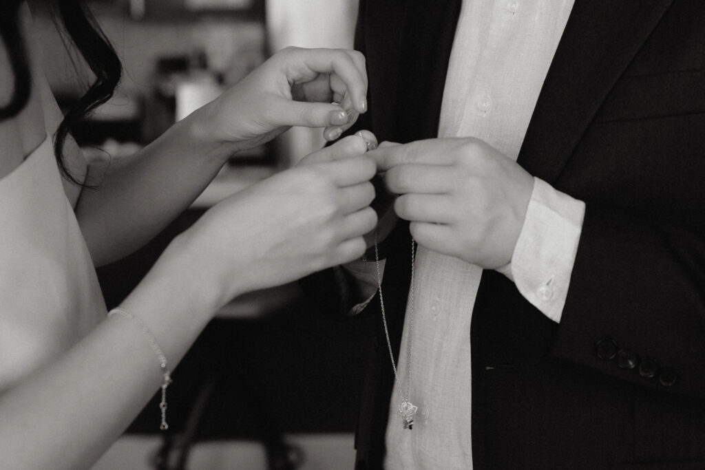 Close-up black and white photo of a couple's hands exchanging a delicate necklace, symbolizing a meaningful moment of connection