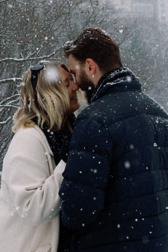 Couple in an intimate moment, smiling and almost kissing, surrounded by snow in a romantic Central Park setting