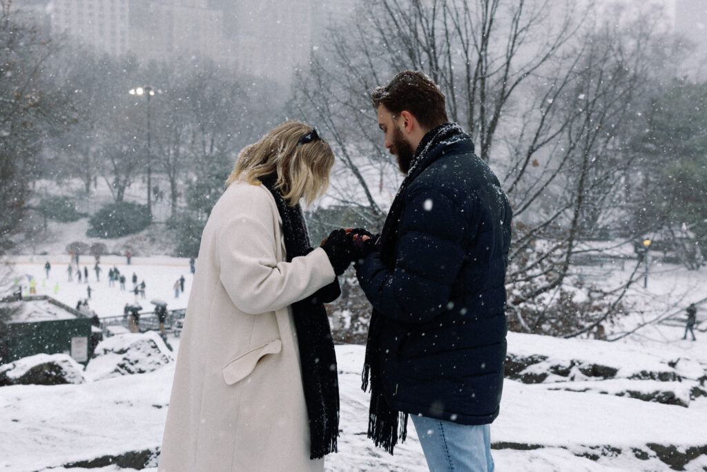 She receives an engagement ring during a proposal in the snow-covered Central Park, a moment filled with love and joy