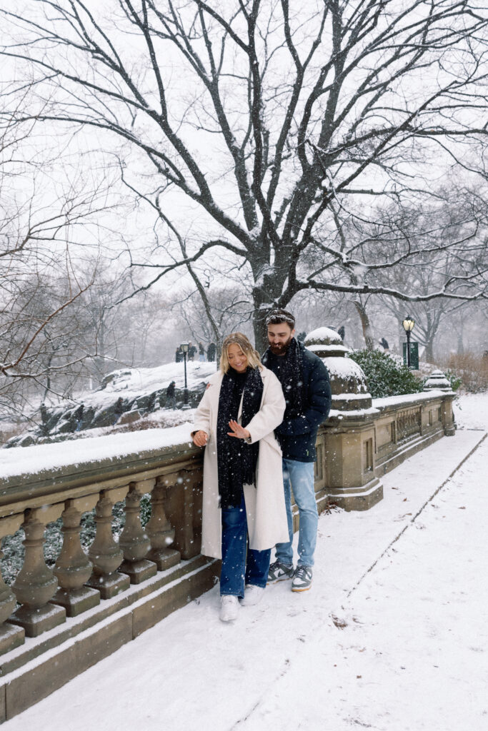 Couple admiring an engagement ring in the snow-covered Central Park, sharing a tender and joyful moment.