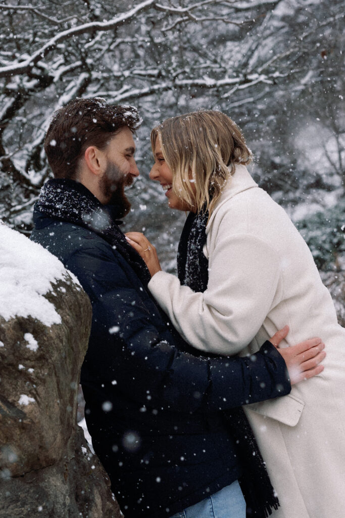 Couple laughing and hugging in the snow-covered Central Park, radiating joy and love.