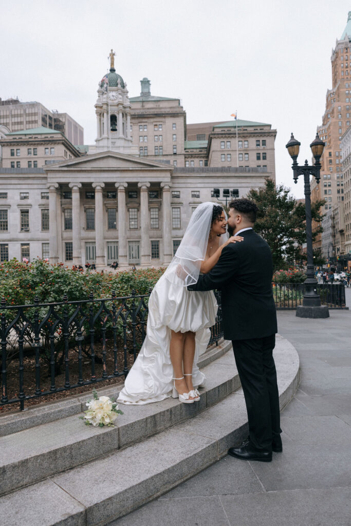 Bride and groom share a romantic kiss in front of Brooklyn Borough Hall during their NYC elopement, with a bouquet resting nearby