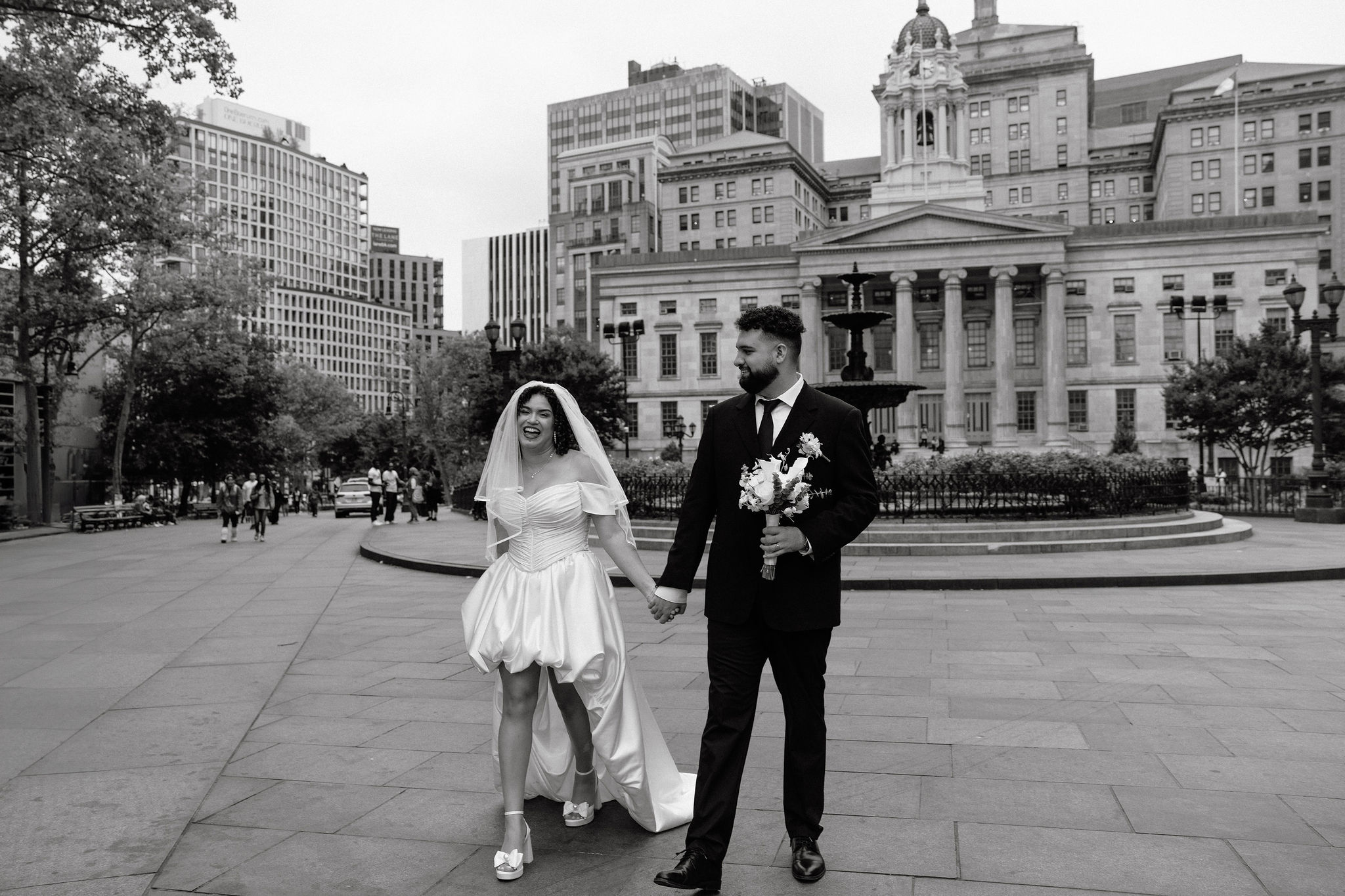 Bride and groom walk hand in hand, smiling and joyful in front of Brooklyn Borough Hall during their NYC elopement