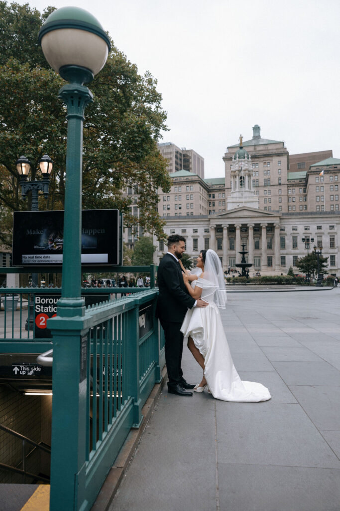 Bride and groom share an intimate moment near the Borough Hall subway entrance with Brooklyn Borough Hall in the background during their NYC elopement.