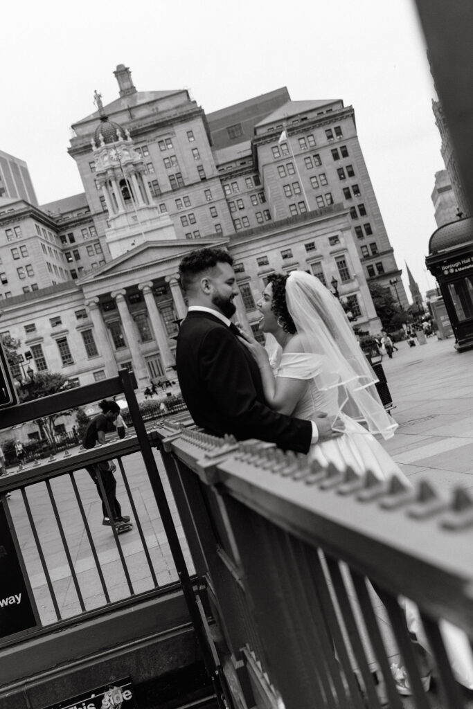 Bride and groom share an intimate moment near the Borough Hall subway entrance in a black-and-white photo with Brooklyn Borough Hall in the background.