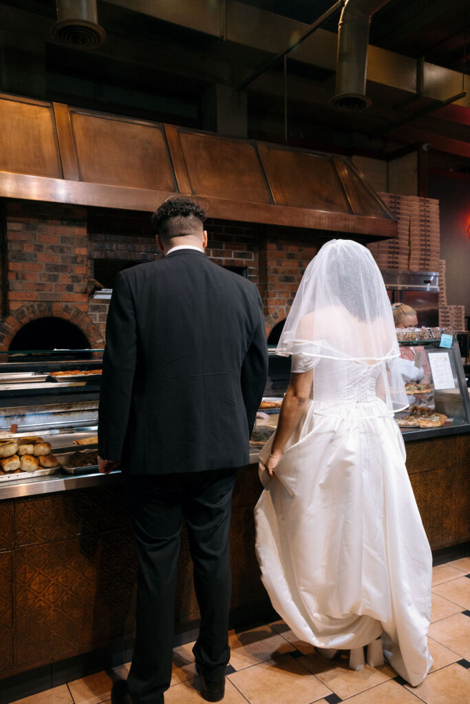 Bride and groom standing at the counter of a Brooklyn pizza shop, sharing a casual and intimate moment after their NYC elopement