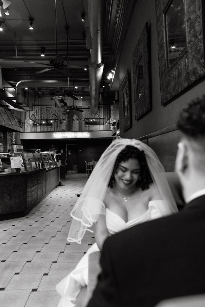 Bride smiling while sitting at a booth in a Brooklyn pizza shop, enjoying a casual moment after her NYC elopement