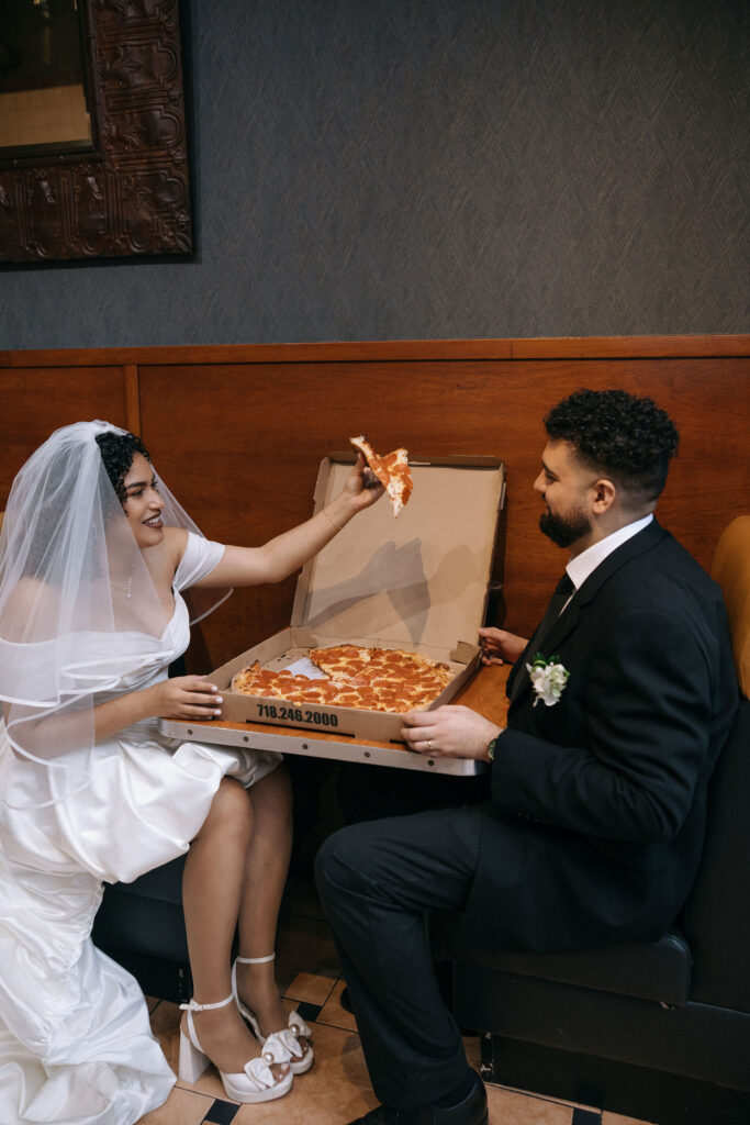 Bride playfully offers a slice of pepperoni pizza to the groom as they celebrate their NYC elopement at a Brooklyn pizza shop