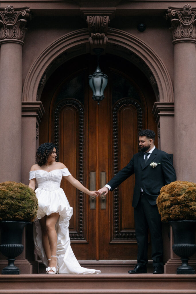 Bride and groom holding hands on the steps of a Brooklyn brownstone, sharing a romantic moment during their NYC elopement.