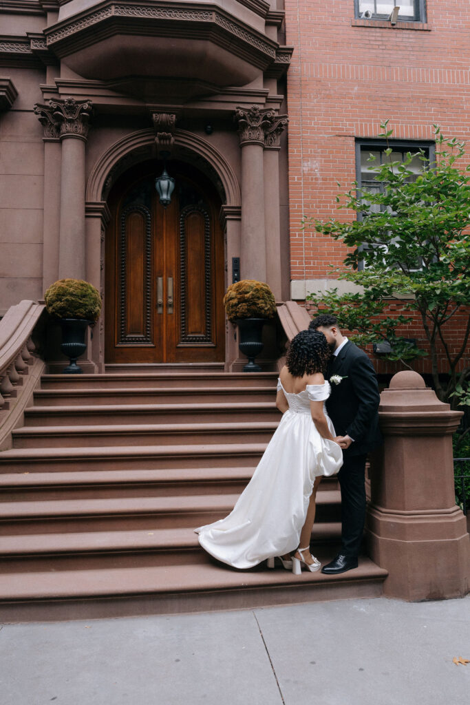 Groom kisses the bride's hand as they share an intimate moment on the steps of a Brooklyn brownstone during their NYC elopement.