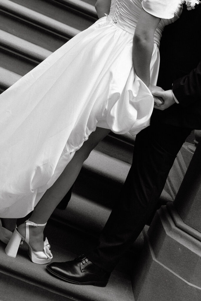 Close-up black-and-white shot of the bride's dress and shoes as she walks up the steps of a Brooklyn brownstone, holding hands with the groom