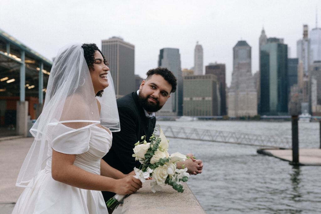 Bride and groom sharing a joyful moment by the waterfront with the Manhattan skyline in the background