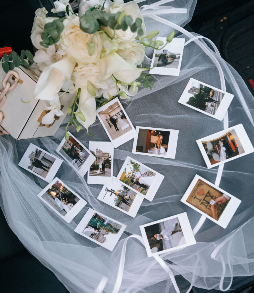 A bridal bouquet of white flowers and eucalyptus resting on a veil, surrounded by a collection of Polaroid snapshots capturing joyful wedding moments