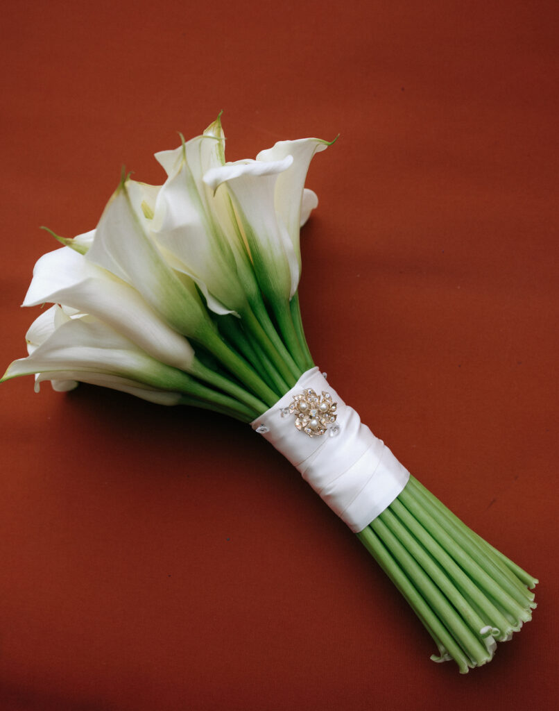 A classic white calla lily bridal bouquet wrapped in satin with a vintage brooch, elegantly styled for a Bowery Hotel wedding.