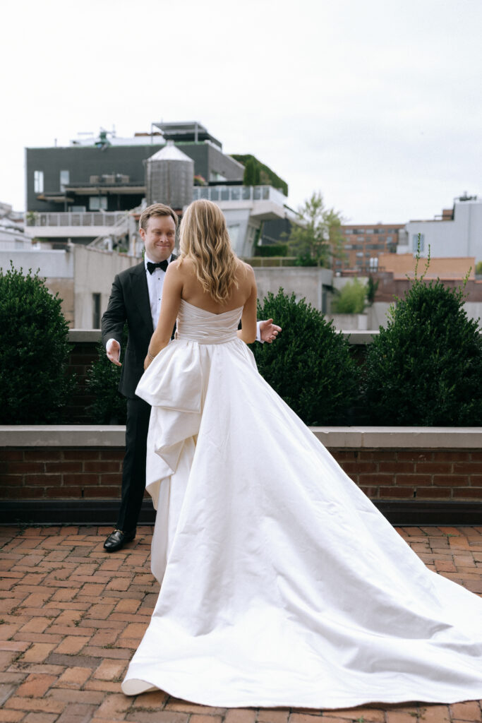 A groom reacts with joy as he sees his bride for the first time during their first look on the rooftop of the Bowery Hotel, with the city skyline behind them.