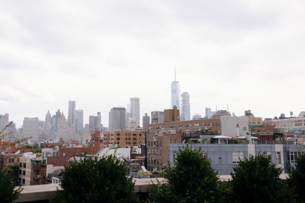 A stunning rooftop view from the Bowery Hotel, showcasing the Lower Manhattan skyline, including One World Trade Center, on a cloudy wedding day.