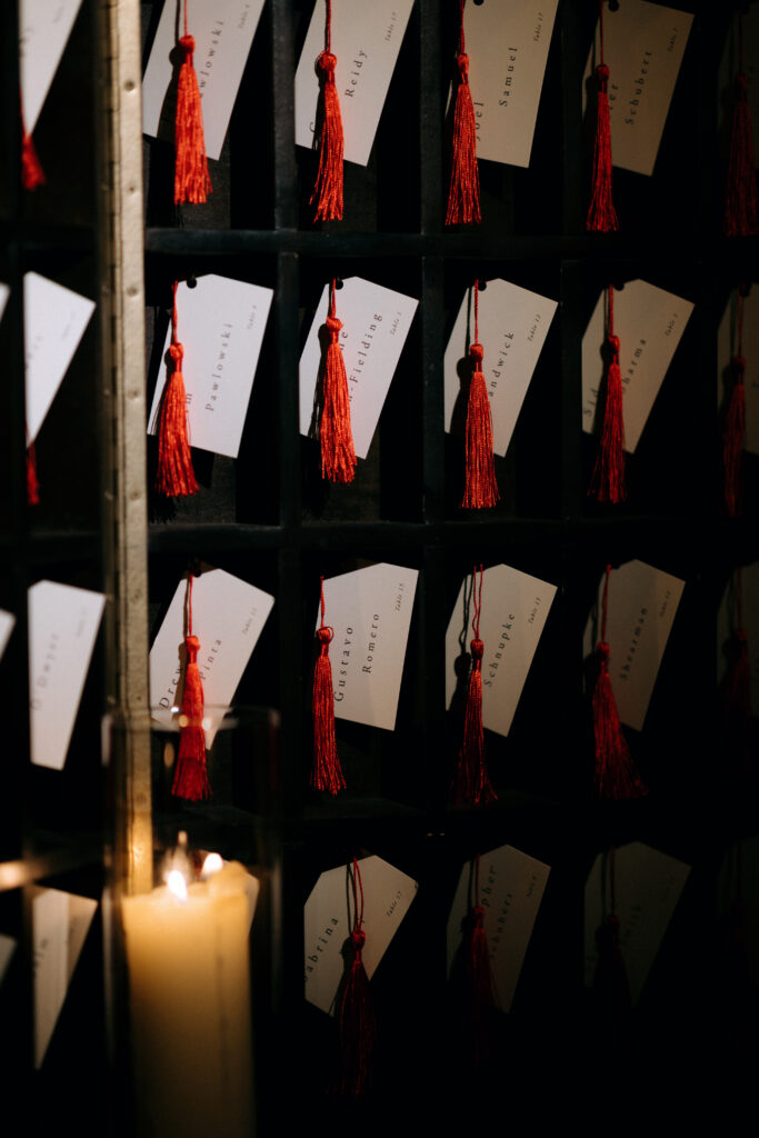 Elegant escort cards with red tassels are displayed in a vintage cubby at the Bowery Hotel wedding, illuminated by the soft glow of candlelight.