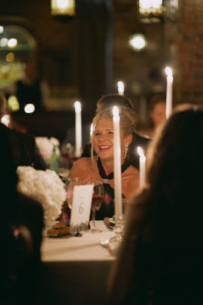 A guest smiles warmly at a candlelit wedding reception at the Bowery Hotel, surrounded by an intimate ambiance of flickering candlelight and elegant table decor.