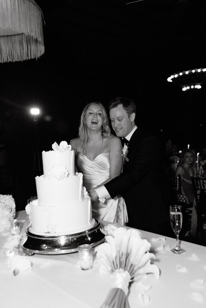 A joyful bride and groom cut their wedding cake at the Bowery Hotel, laughing together in a beautifully candid black-and-white moment.