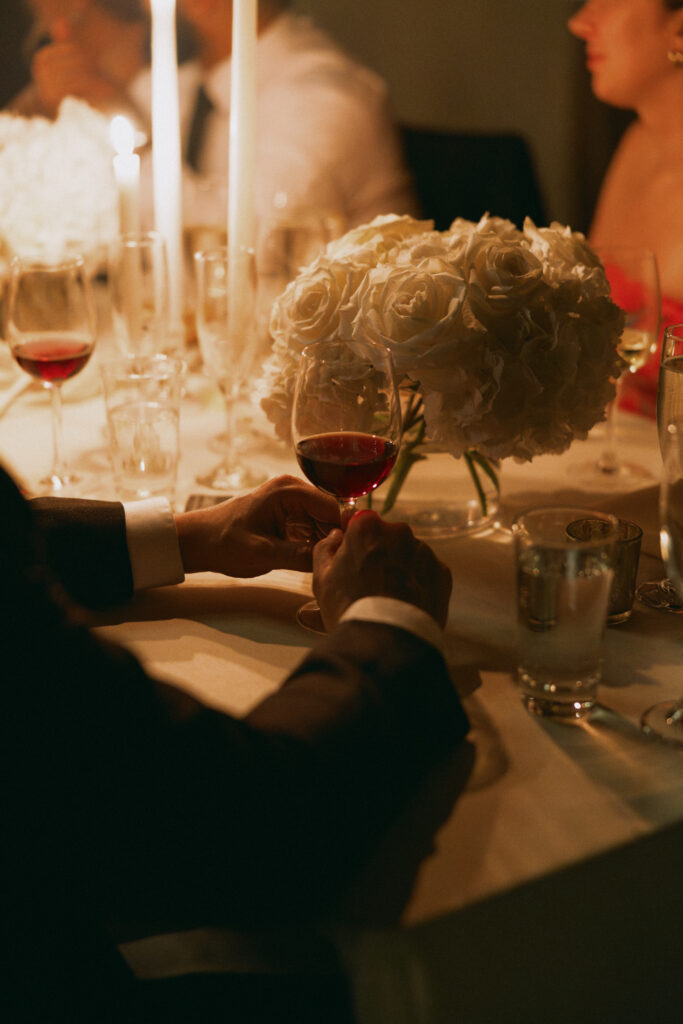 A romantic candlelit wedding reception at the Bowery Hotel, featuring an intimate table setting with white roses, wine glasses, and soft lighting.