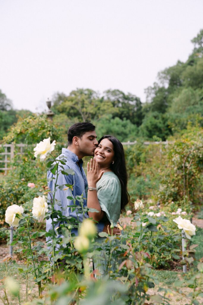 Engaged couple kissing in the Rose Garden at Brooklyn Botanic Garden, captured by NYC proposal and engagement photographer Yelena Ku.
