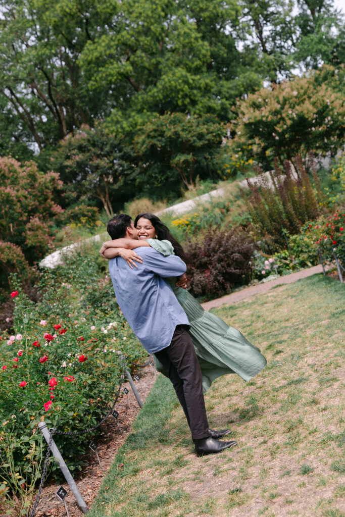 Groom-to-be lifting his fiancée in the Rose Garden at Brooklyn Botanic Garden after their surprise proposal, captured by NYC engagement photographer.
