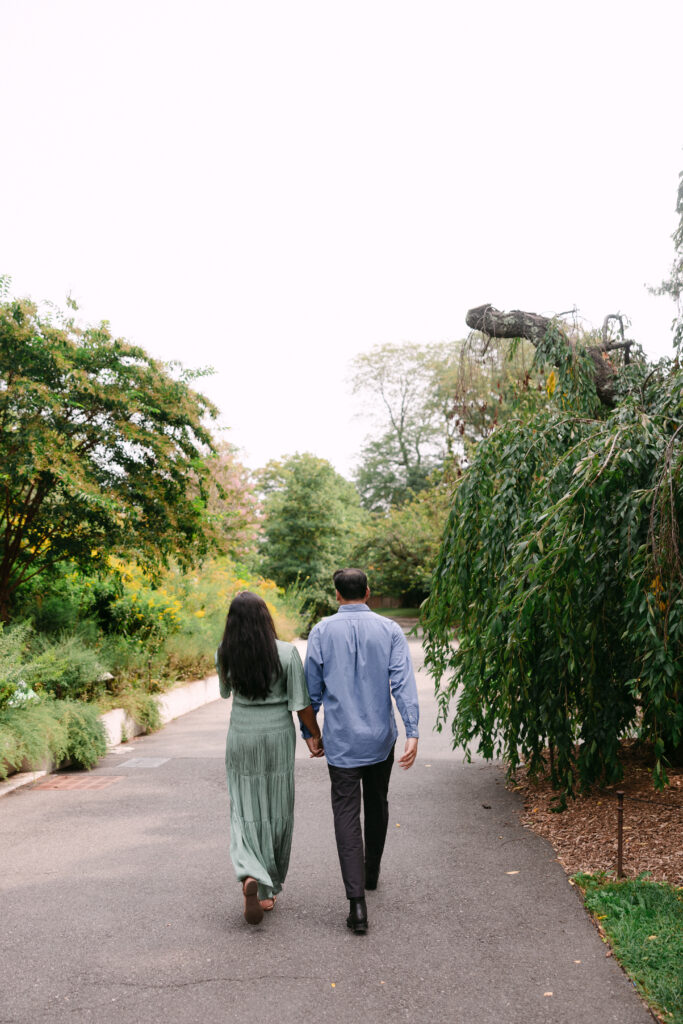 Engaged couple walking hand in hand down a garden path at Brooklyn Botanic Garden after their proposal, captured by NYC engagement photographer.
